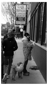 black and white photo of a woman walking a dog on a sidewalk