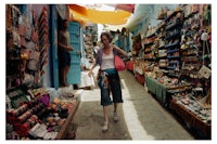 a woman walking down a narrow alley full of merchandise